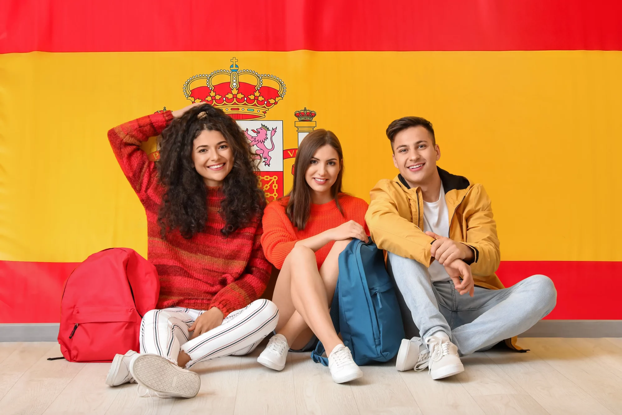 Three young people sitting in front of the flag of Spain